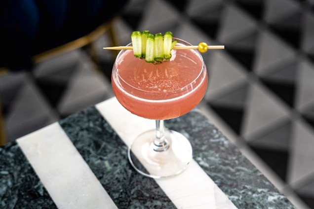 A vibrant cocktail with cucumber and a stylish garnish on top, presented at Plume in Houston, TX.